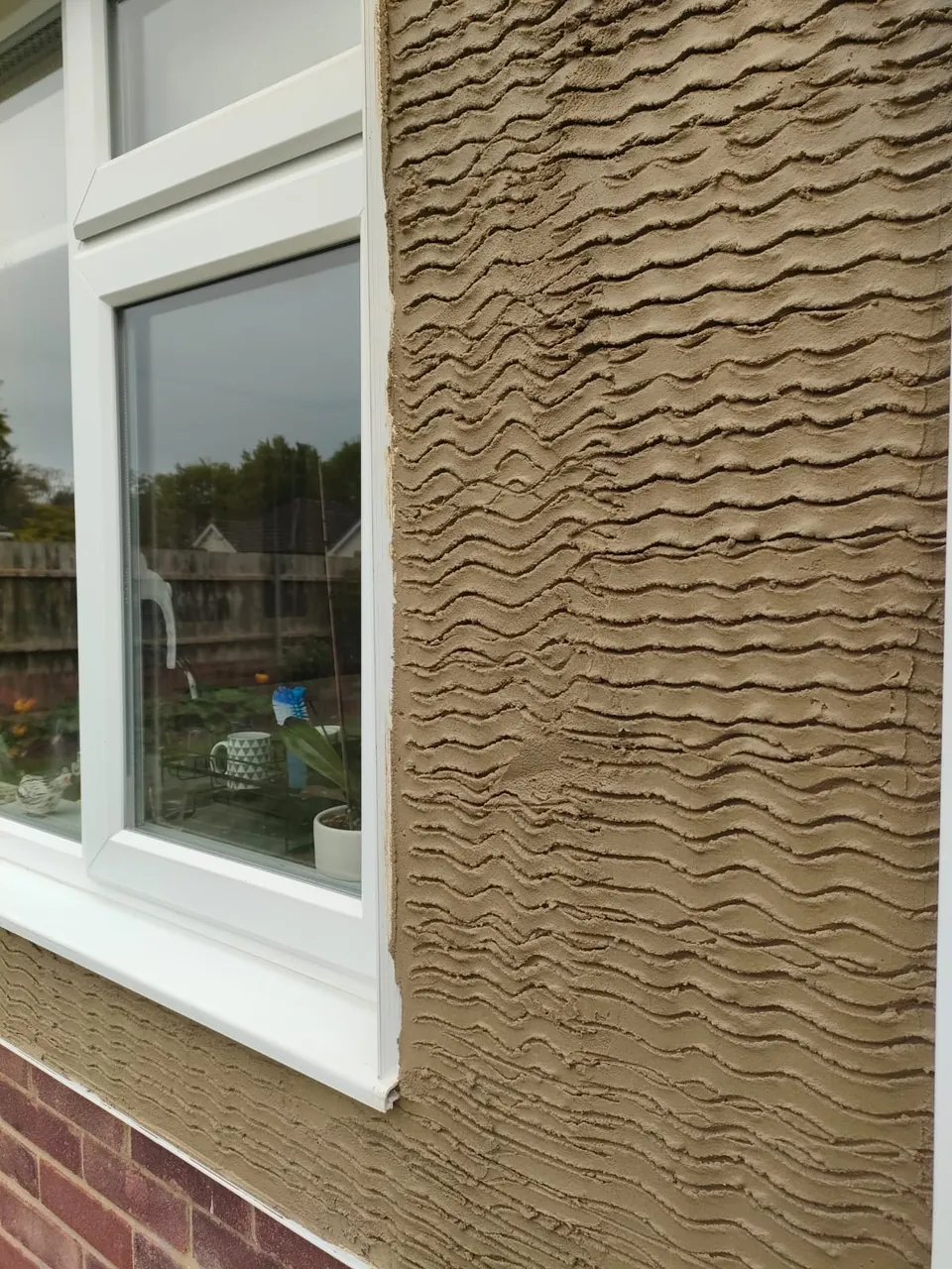 Close-up of the scratch coat of render beside a white window