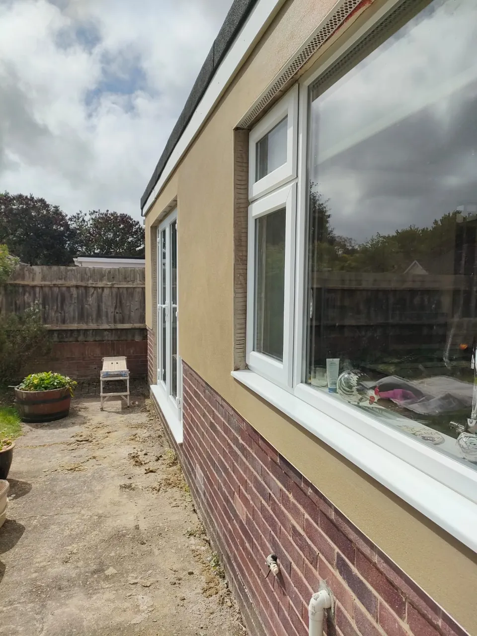 Finished smooth render beside a white window on a bungalow with a brick plinth