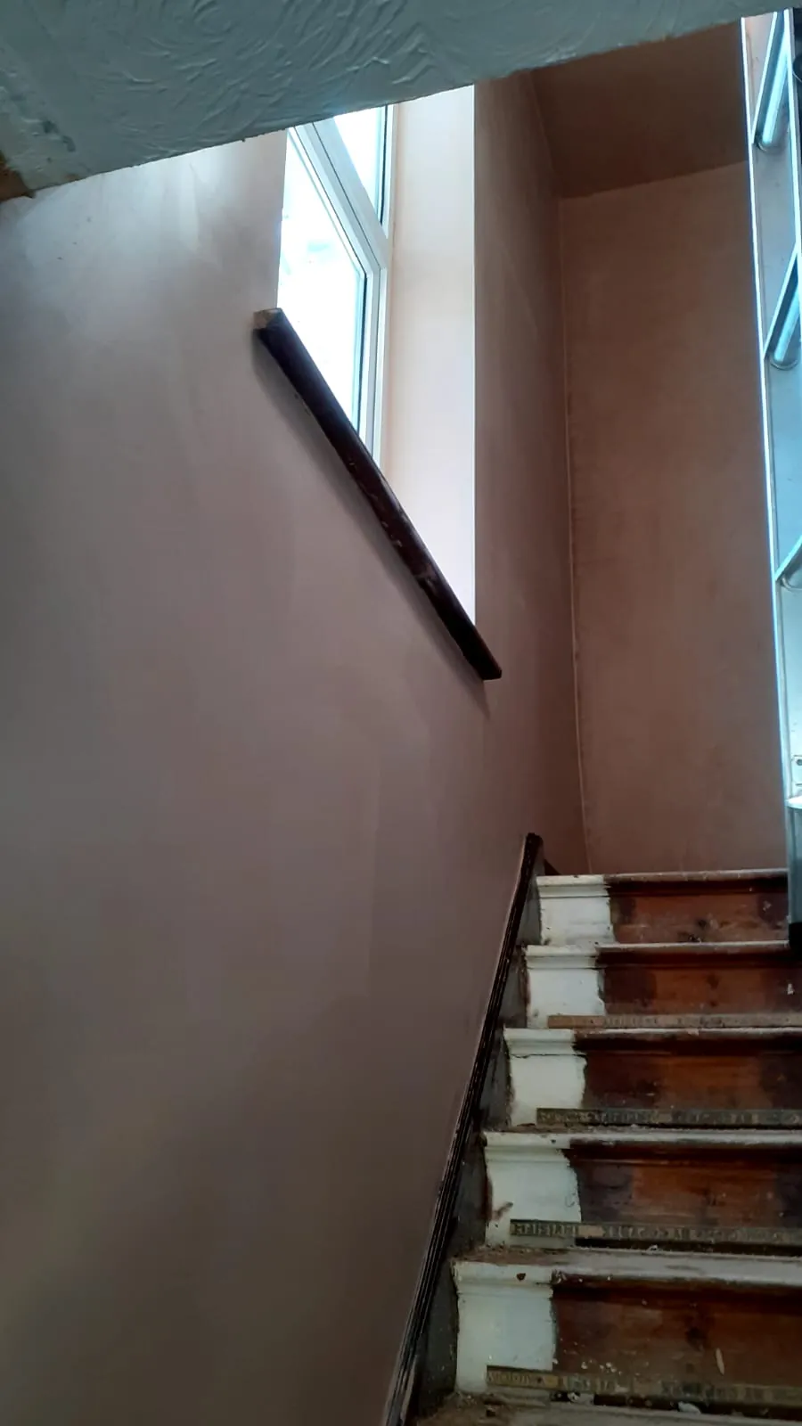 Newly plastered stairwell walls around a window above the stairs