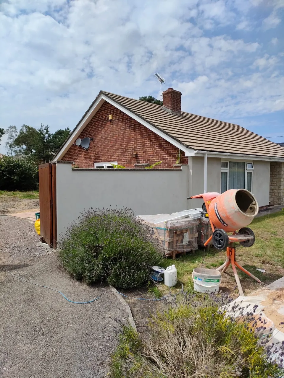 Smooth finished render on a garden wall and the side of a brick bungalow, with a cement mixer and lavender in front