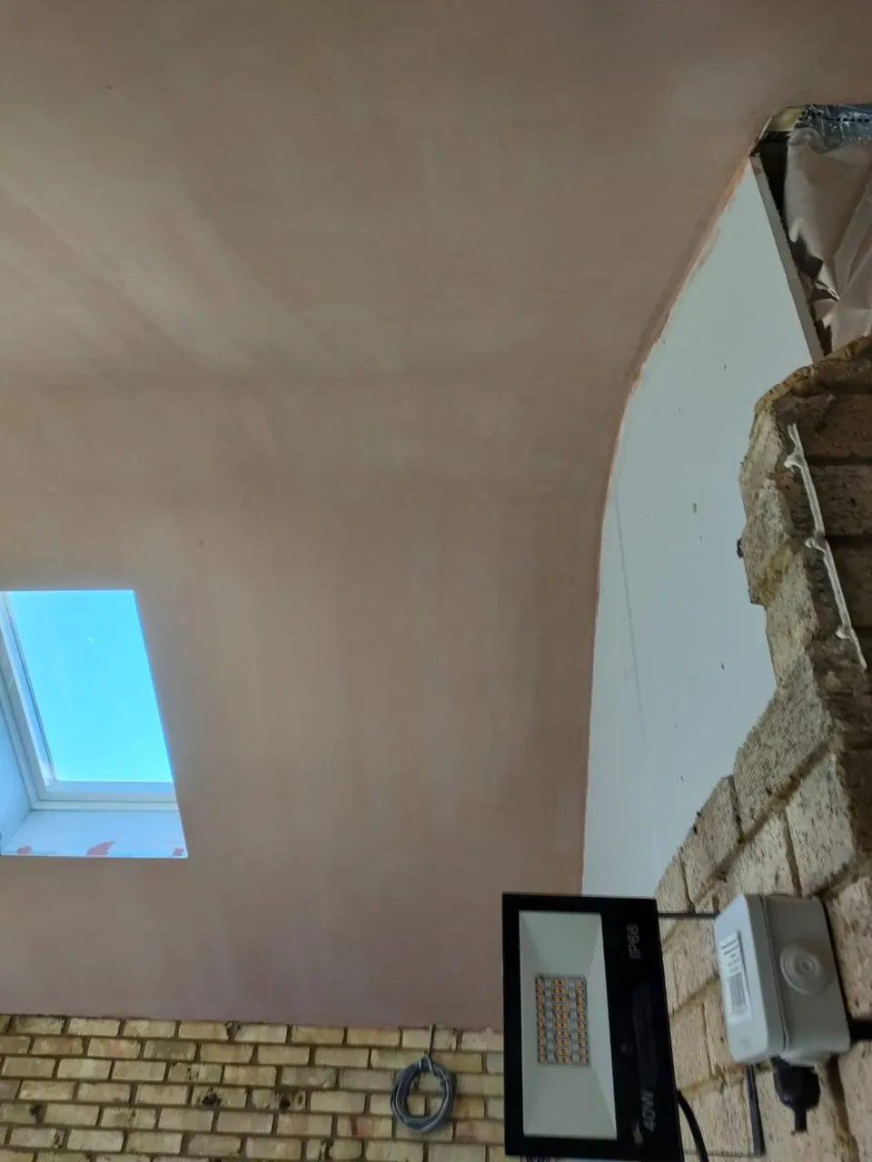 Skimmed vaulted ceiling with a roof window above an exposed yellow brick wall