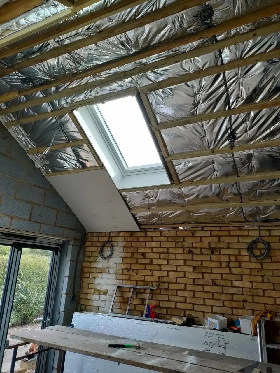 Roof rafters lined with foil insulation around a roof window before the ceiling was boarded